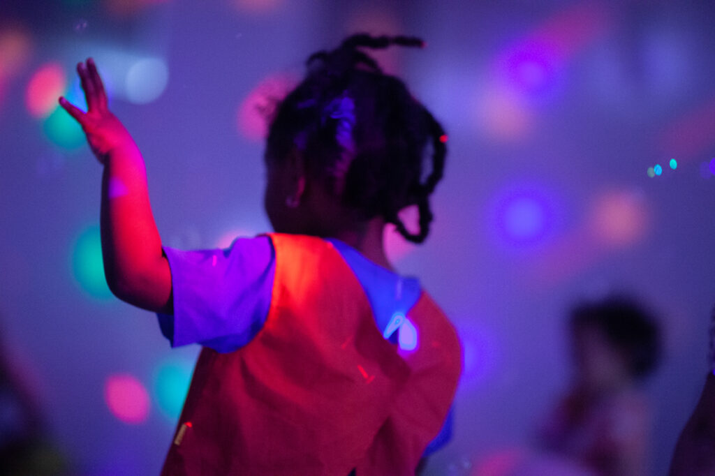 Bild i mest lila av ett barn som dansar i skenet av en diskokula