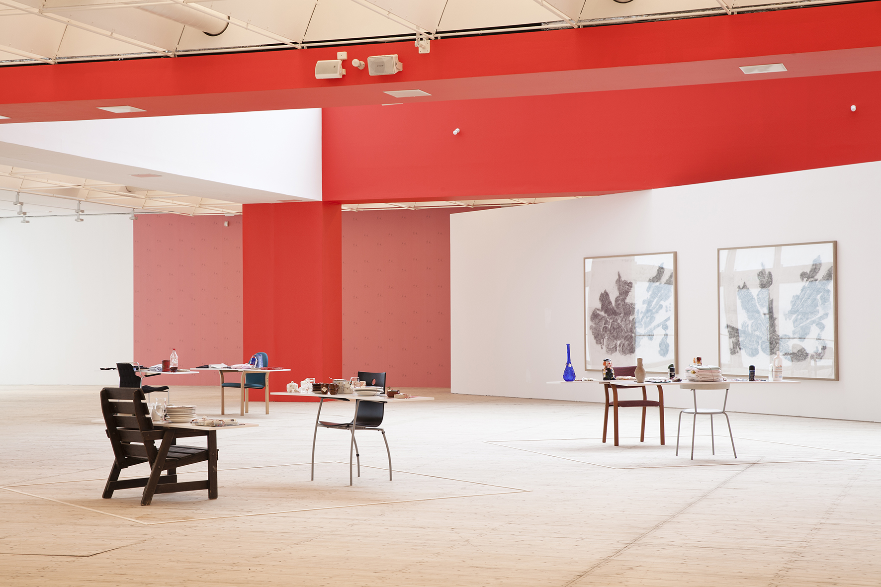 Installation picture from inside the art hall. The walls are painted in a vibrant red color, and artworks are scattered throughout the room.