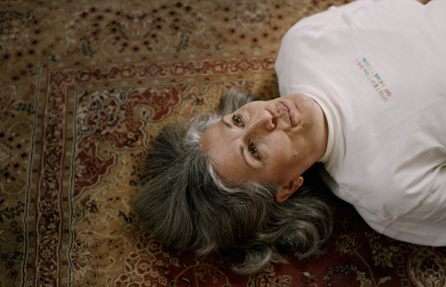 Image from the movie 'A Magical Substance Flows Into Me', gray-haired woman lying on a Persian rug.