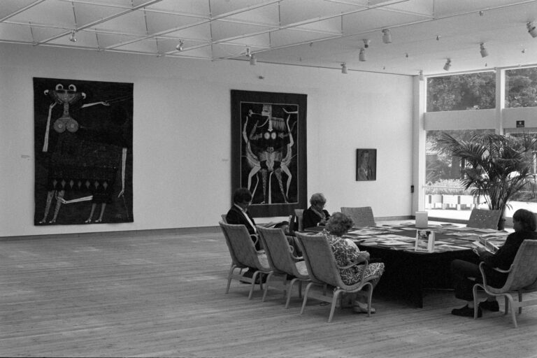 Besökare sitter vid ett stort bord och bläddrar bland bilder och böcker i Max Walter Svanbergs utställning 1979.