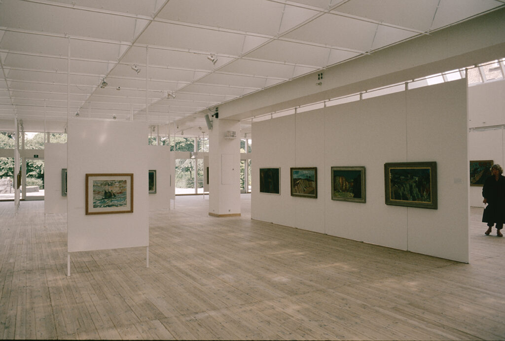 Målningar, klassiskt upphängda på rad i konsthallsrummet.