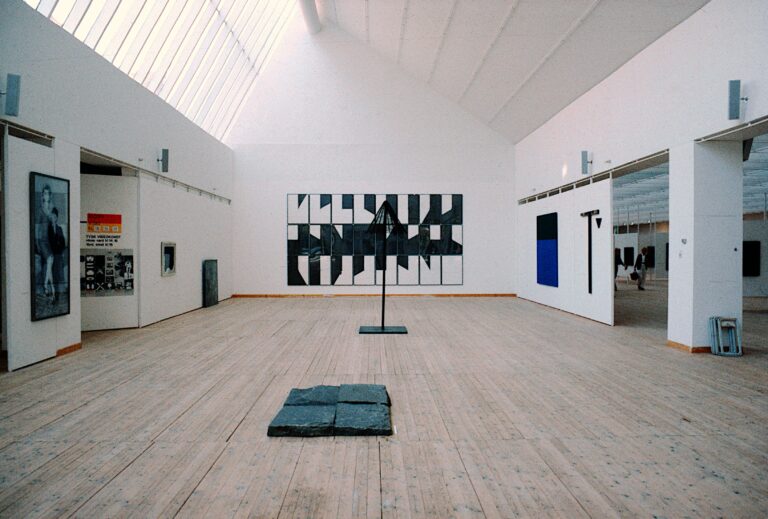 Ett ljust rum i en konsthall med ljusa väggar och trägolv.