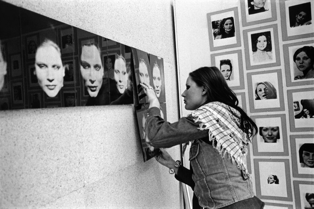Young woman wearing a Palestinian shawl fine-tunes her artwork on the wall.