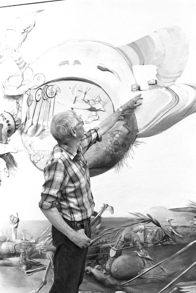 Sven Erik Johansson står framför en av sina stora målningar och pekar på en detalj i bilden.