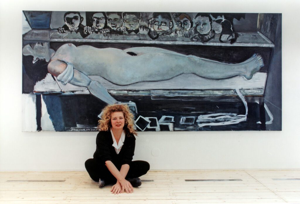 Marlene Dumas sitter med korslagda ben framför en av hennes målningar med en liggande naken kvinna