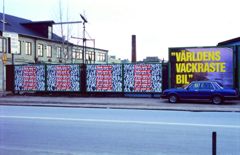 Barbara Kreugers verk täcker en vägg vid en bilväg. Till höger i bild står en bil parkerad på trottoaren.