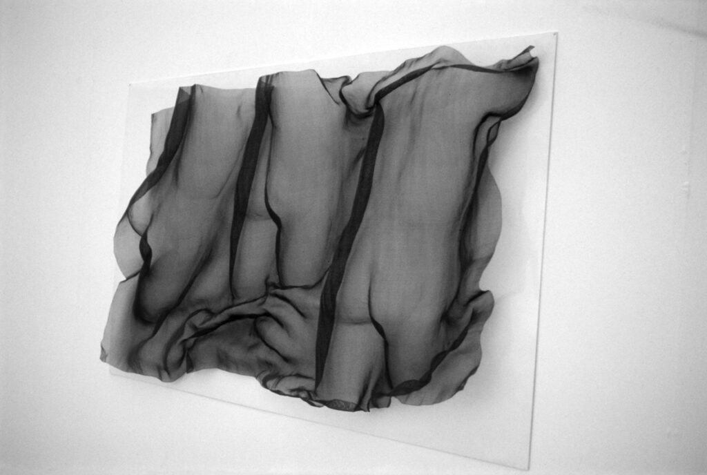 Ett textilverk av Barbro Bäckström, svart, styvt, genomskinligt tyg installerat på en vit bakgrund.