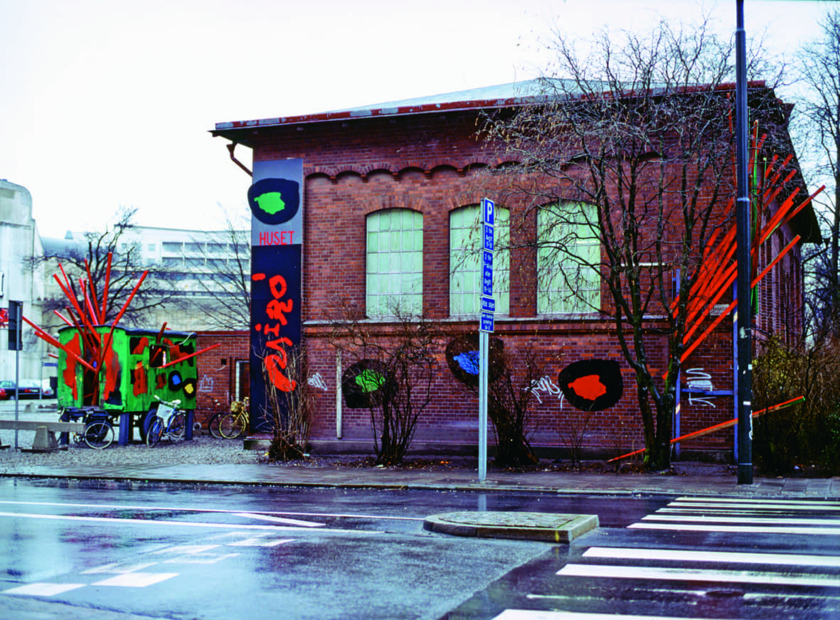 Bild på Joan Miró-huset. Ett stort tegelhus med stora fönster som är målade i ljust grön färg. Till höger i bild syns ett kalt träd. Till vänster står några cyklar parkerade.