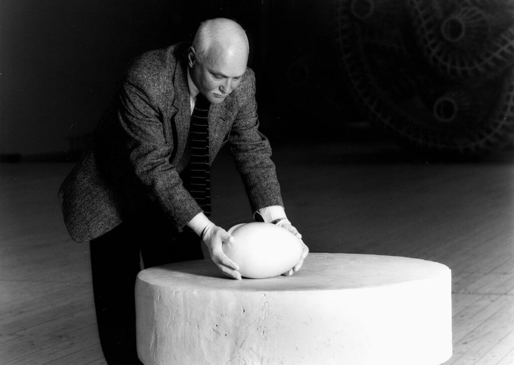 Constantin Brancusi ställde ut ett verk i form av en marmorskulptur. I bild syns museets dåvarande chef Björn Springfeldt som med varsamma händer placerar marmorskulturen på ett postament. Björn är iklädd skjorta slips och kavaj, han tittar ner på skulpturen medan han placerar den.