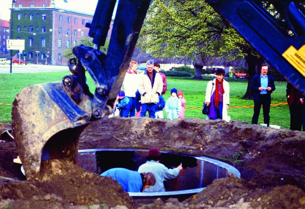 Två personer står i en uppgrävd cirkel i Magistratsparken utanför Malmö Konsthall. I förgrunden av fotot syns en grävskopa från en grävmaskin. Några personer står runt om och tittar ner på personerna som jobbar i gropen.