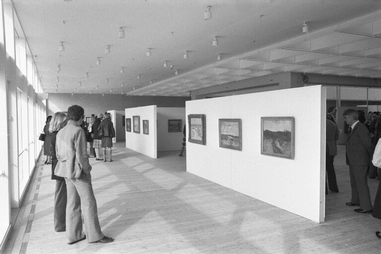 Carl Fredrik Hills verk hänger på vita väggar ut mot magistratsparken. Besökare betraktar målningarna.