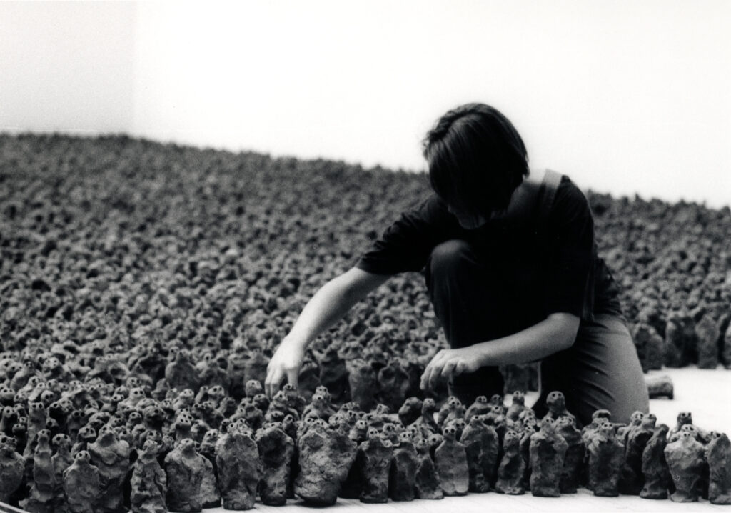 A person crouching down, organizing hundreds of small clay figures.