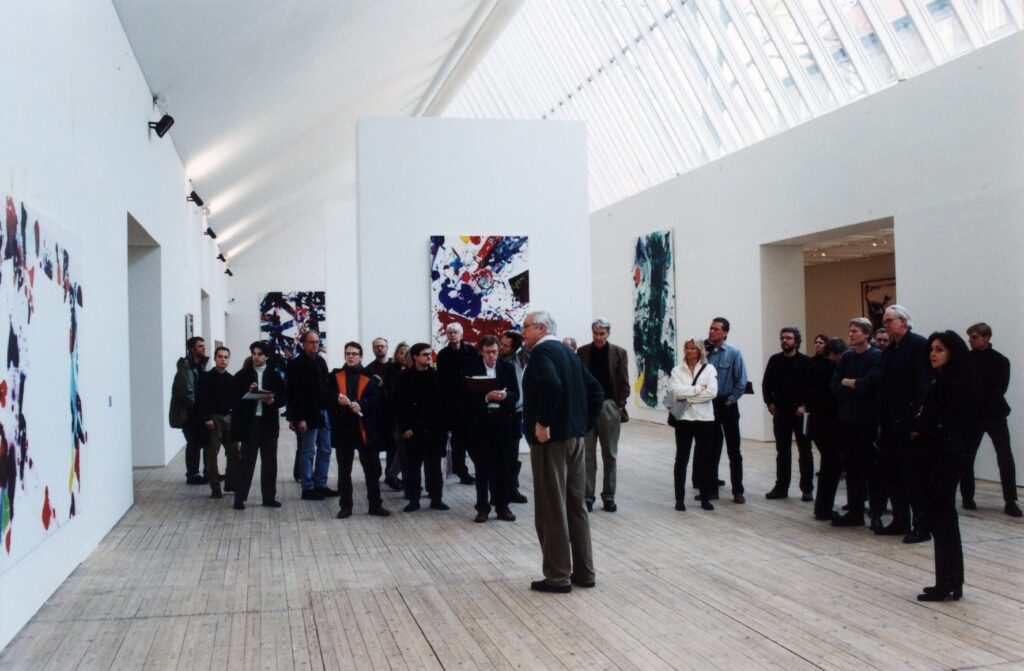 Färgstarka målningar av Sam Francis, upphängda på väggar i en konsthall med ljusa väggar och trägolv. En stor grupp besökare står samlade i rummet och tittar på verken.