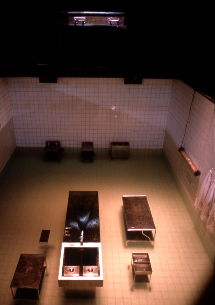 Installationsvy av Peter Greenaways verk, bestående av ett nedsänkt, kaklat rum, sett från ovan, där bänkar och bord är placerade.
