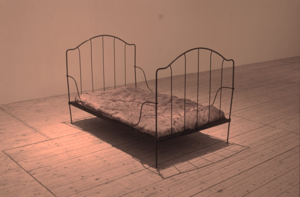 Skulptur av Jana Sterbak. En späd, men elegant säng i svart metall. Sängen har en madrass som ser smutsig ut.