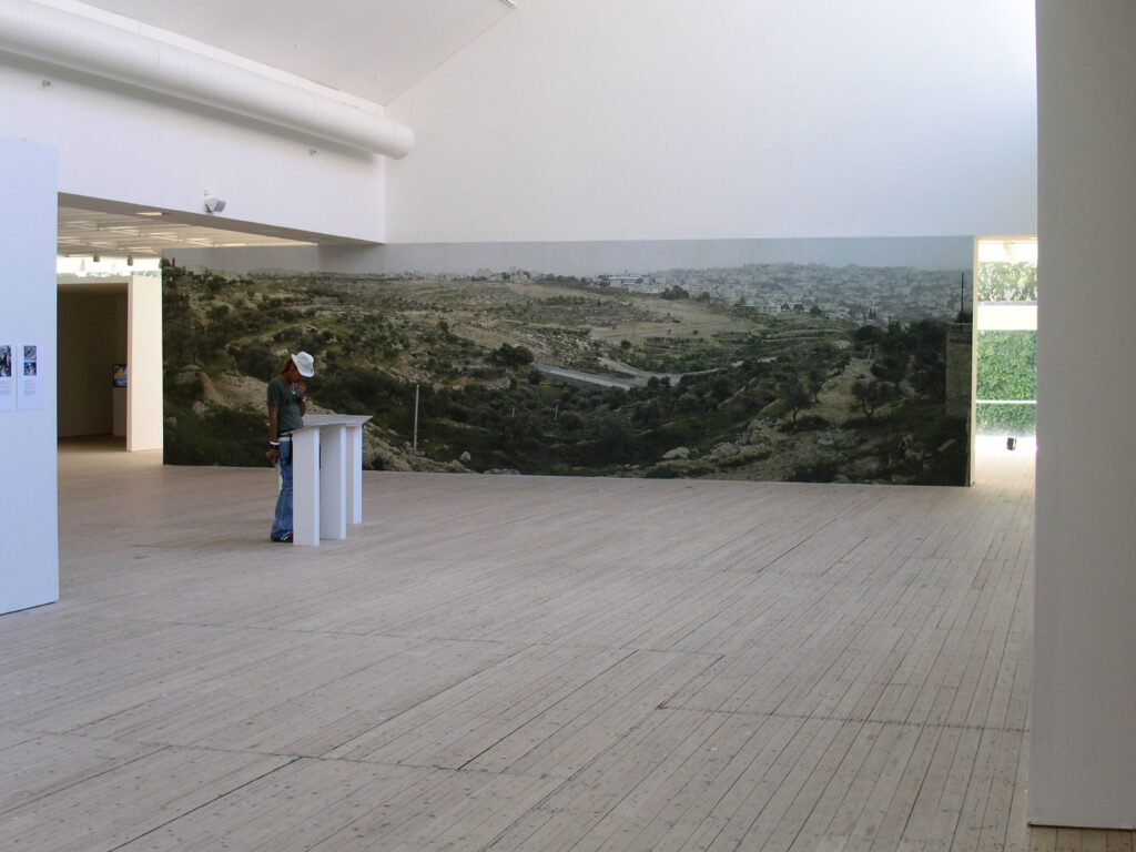 Installationsbild/vy av utställningen Territories 2004. Ett gigantiskt fotografi av ett landskap klär en lång vägg i utställninsrummet.