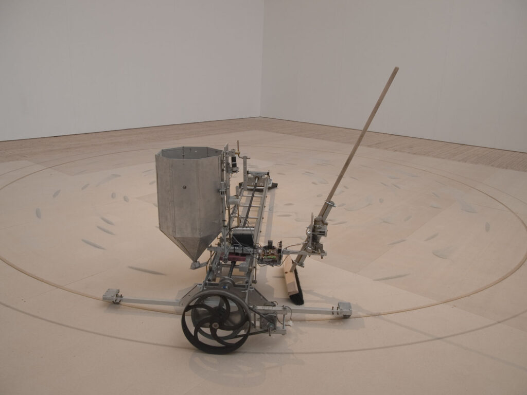 Installation som del av utställningen Electrohype 2008. En märklig maskin bestående av bland annat en sopkvast, hjul, en lång arm i metal och en behållare i metall.