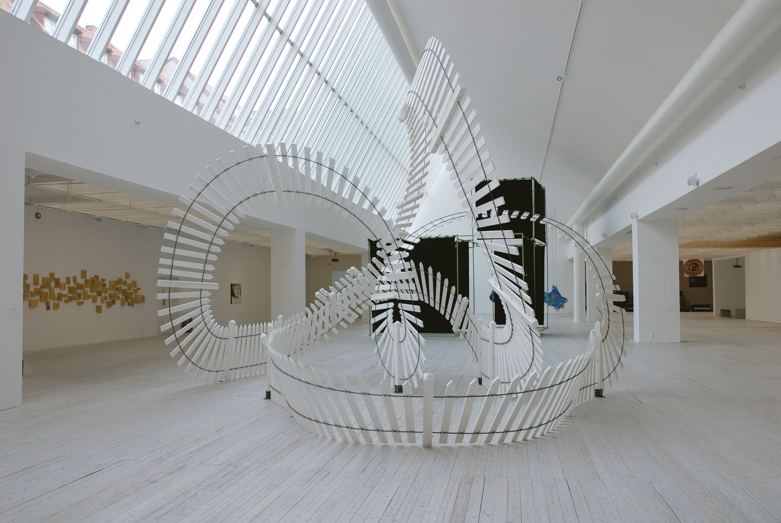 Ett vitmålat staket som är format till en stor formation som en berg- och dalbana. Skulpturen står i ljusschaktet.