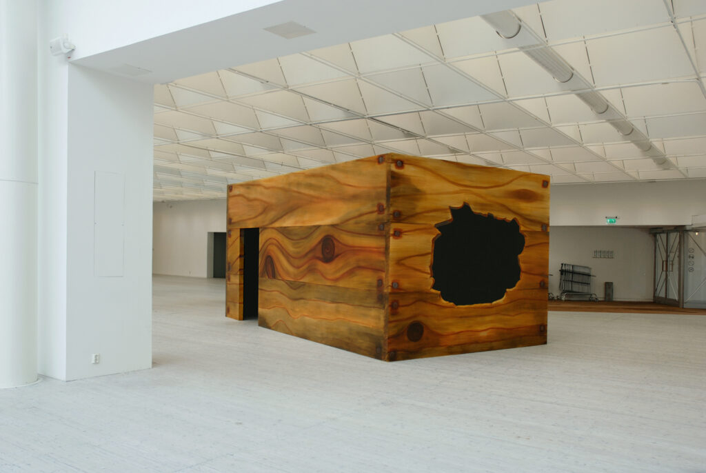 Ett kvadratiskt rum som är målad som en liten trälåda på utsidan. Rummet blir till en skulptur.