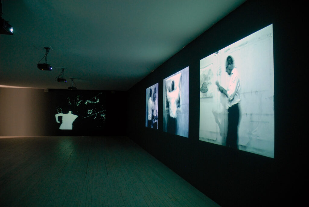 Installationsbild från utställningen William Kentridge. Ett flertal projektioner på väggarna i ett mörklagt rum.