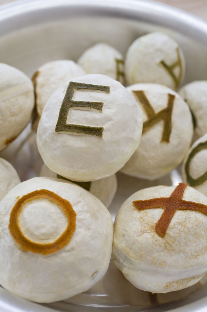 Runda vita objekt ligger i en skål. Det finns en bokstav på varje objekt.