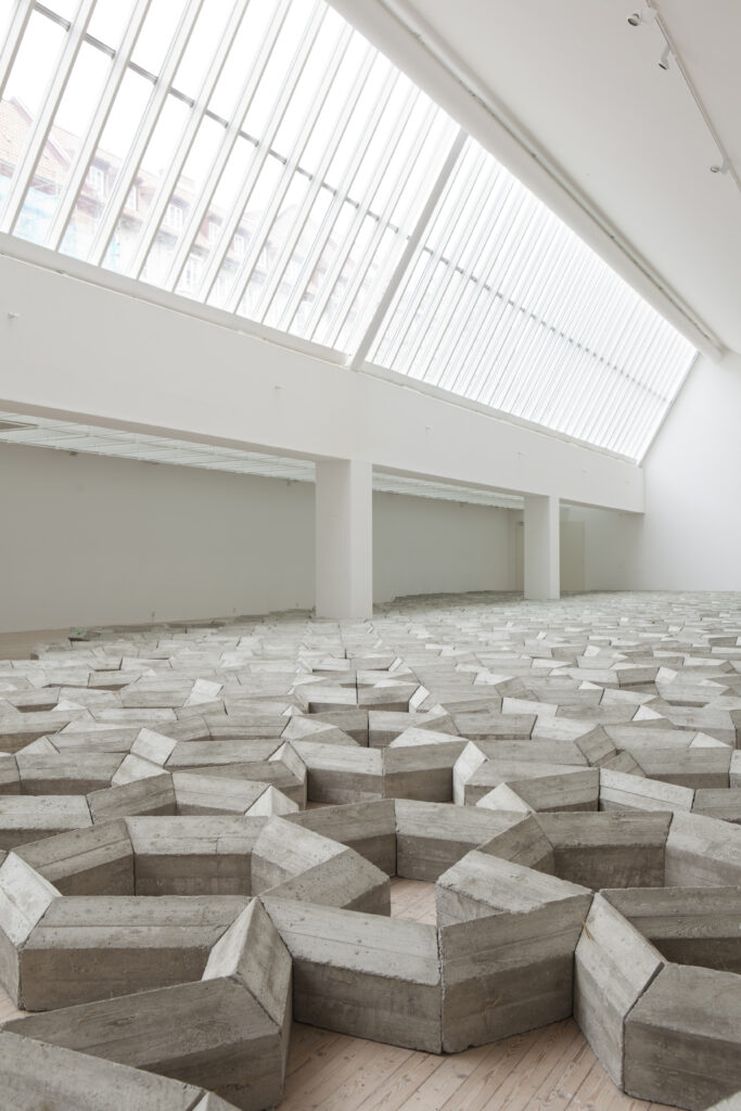 En installation av Mike Nelson i form av ett betongverk breder ut sig över konsthallens golv.