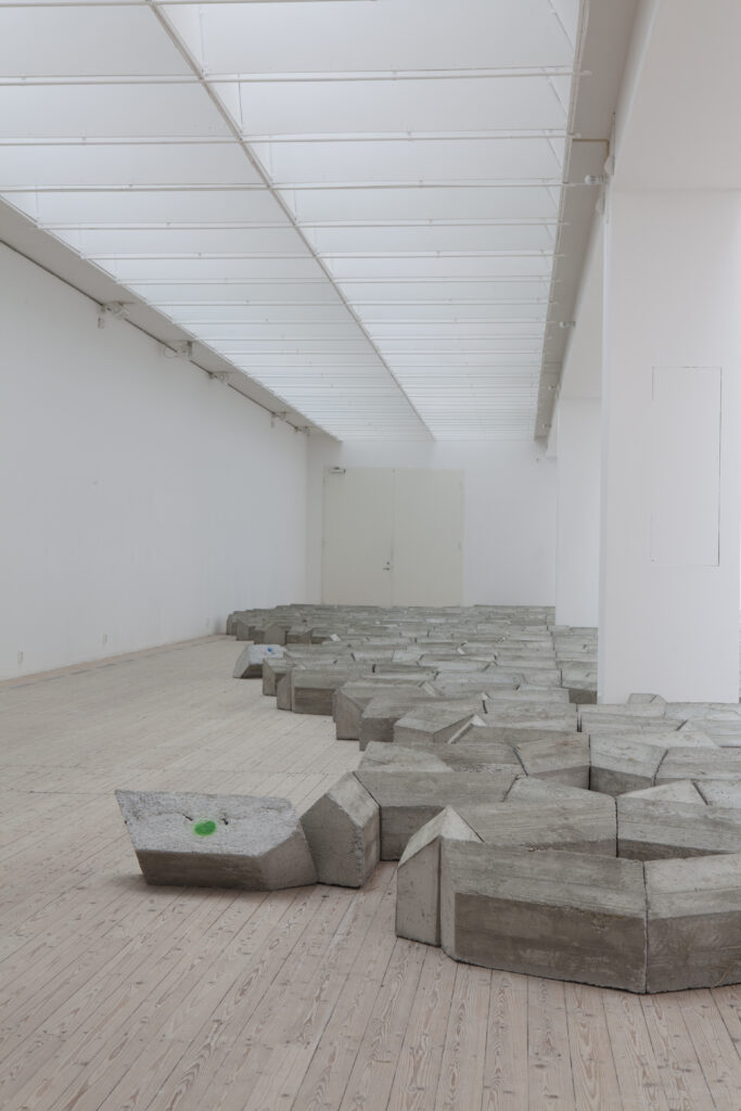 En installation av Mike Nelson i form av ett betongverk breder ut sig över konsthallens golv.