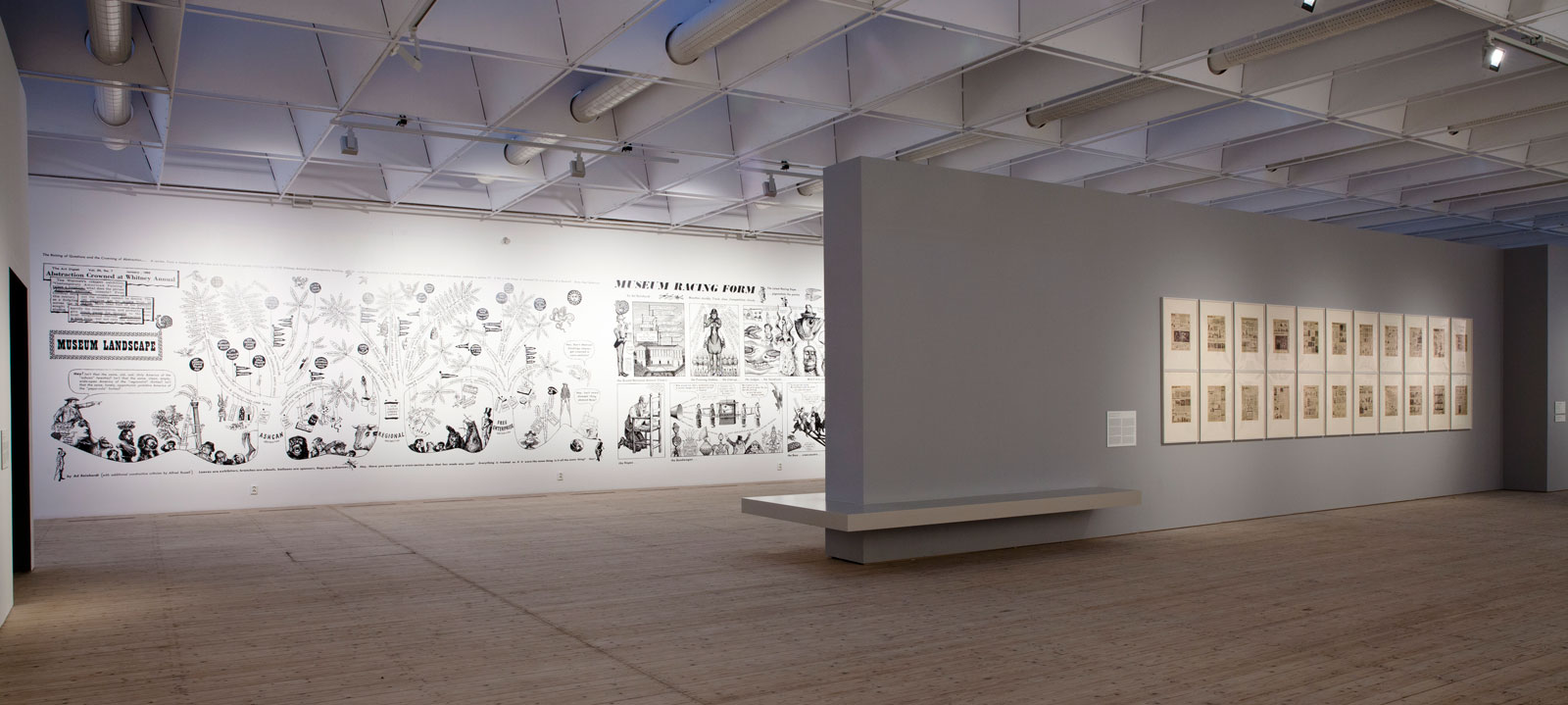 Översiktsbild av utställningen Ad Reinhardt, 2015. Stora serieteckningar är tapetserade på en lång vägg och mindre inramade verk på en annan.