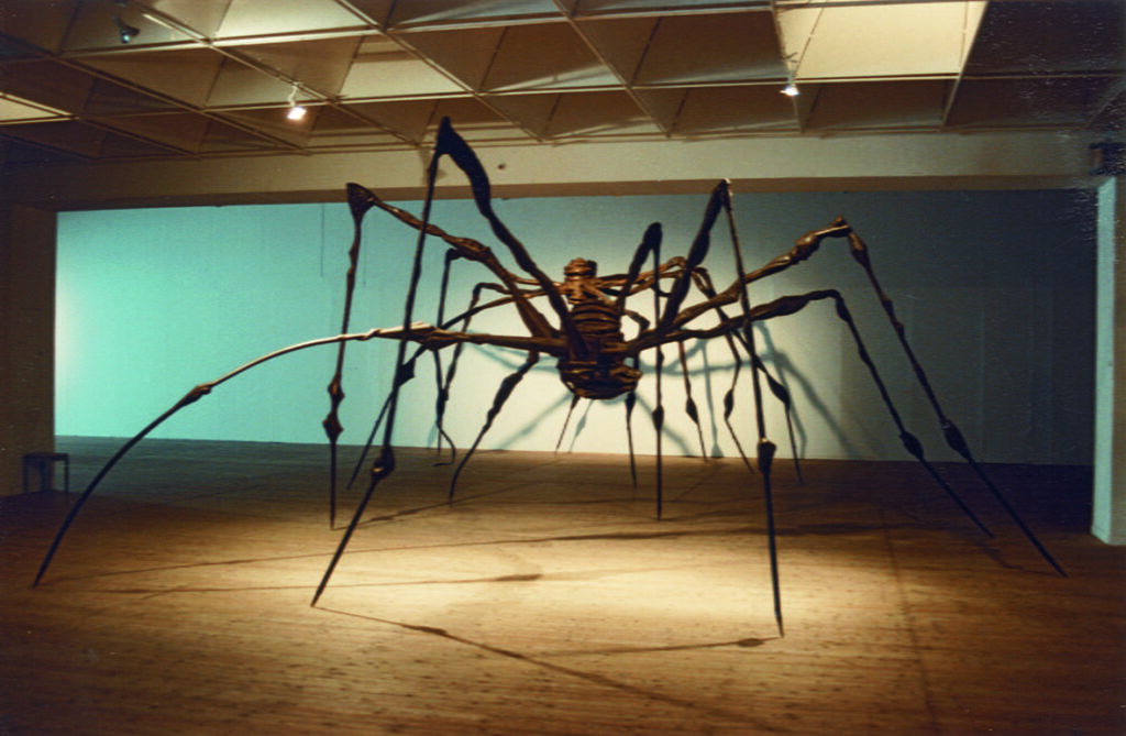 En stor spindelliknanade skulptur, belyst med lampor uppifrån.