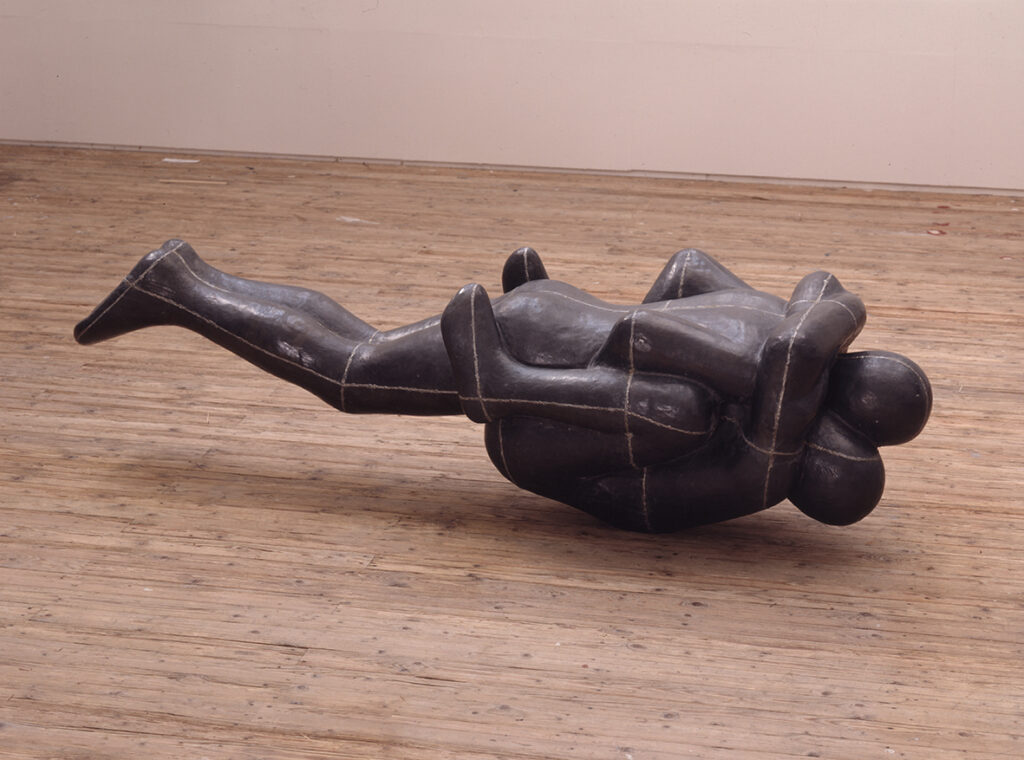 Skulptur föreställande två människor. Den ena ligger raklång ovanpå den andra som har sina knän uppe i armhålorna.