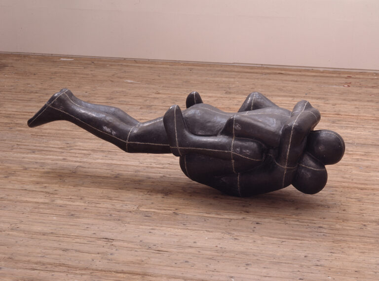 Skulptur föreställande två människor. Den ena ligger raklång ovanpå den andra som har sina knän uppe i armhålorna.