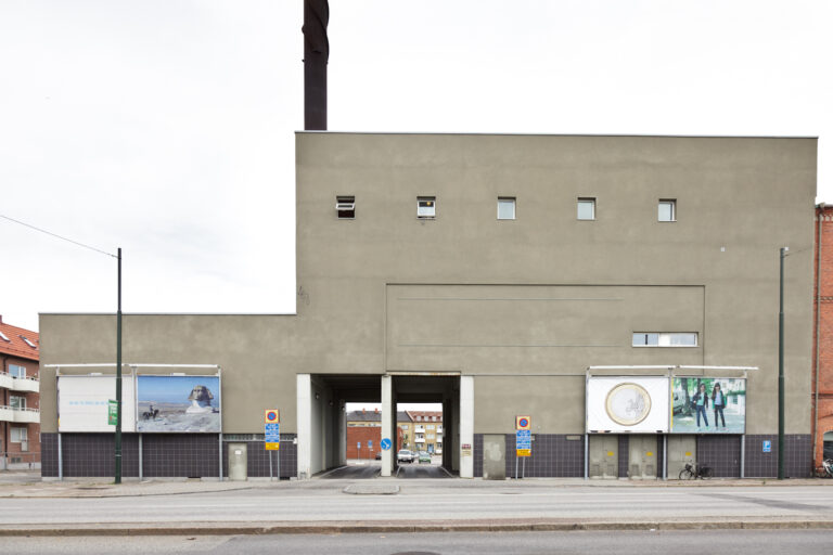 Fyra stycken billboard-tavlor på en grå fabriksliknande byggnad.