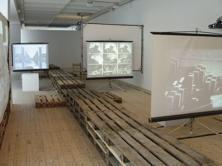 Installationsbild av lastpallar och diabildsskärmar inne i konsthallen.