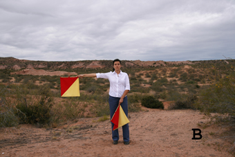 Kvinna står i torrt landskap med två gul och röda, kvadratiska flaggor.