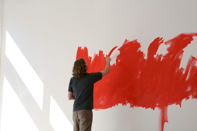 Konstnären David Shrigly målar rött på en vit vägg i konsthallen.