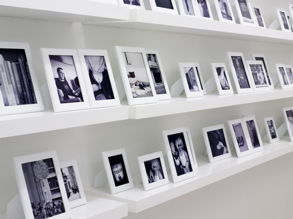 Installation av Elmgreen och Dragset. Rader av inramade bilder står på vita vägghyllor.