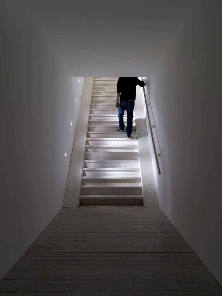Installation av Elmgreen och Dragset. En man går upp för en trätrappa, längst in i ett smalt rum.