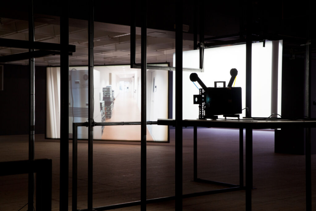 En stor metallkonstruktion med en äldre filmprojektor syns i förgrunden. I bakgrunden anar man filmprojektioner.