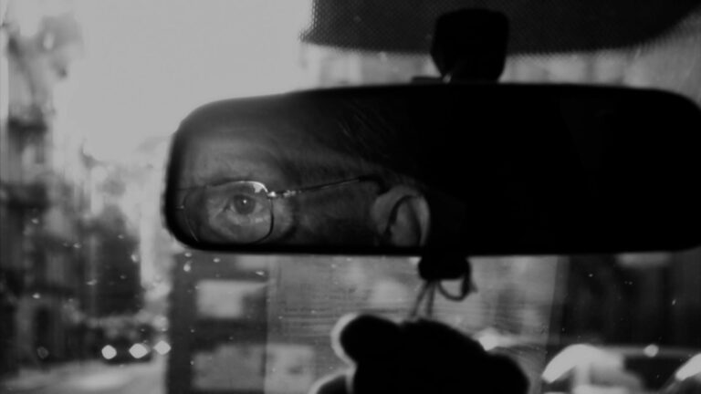 svartvit bild av backspegel där man ser ögat av mannen som kör