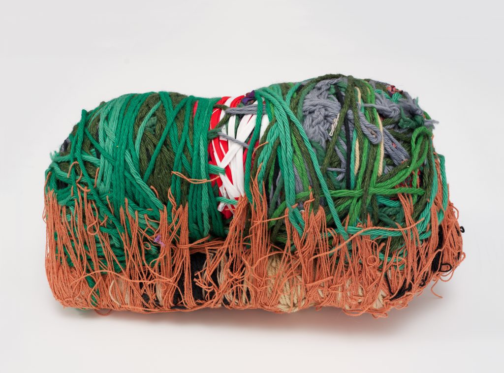 Konstverk av Judith Scott i garn och tråd som har snurrats i en organisk form. Färgerna är orange och grönt.