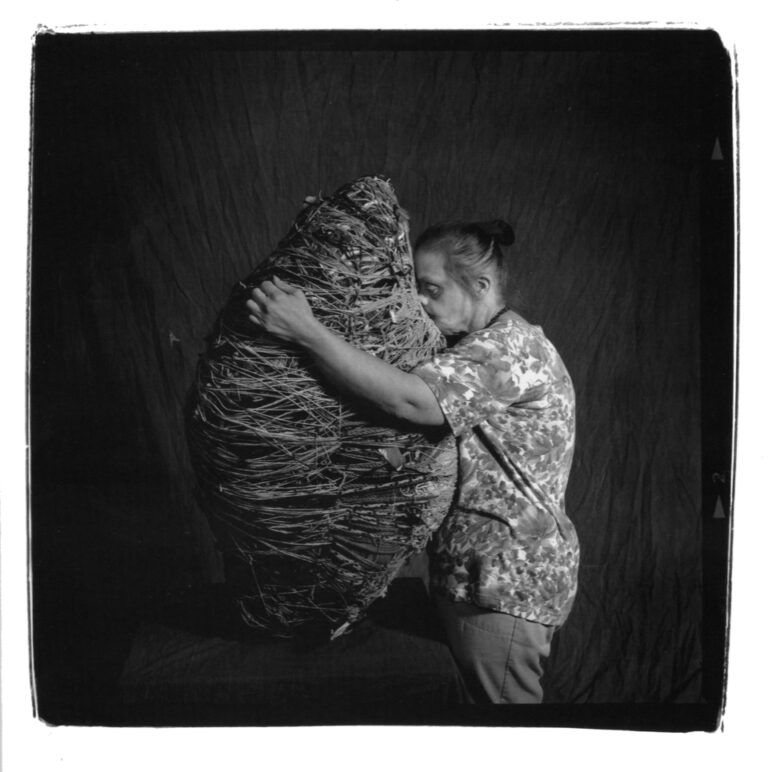 Fotografiskt porträtt av Judith Scott. Hon kramar en av sina organiska skulpturer.