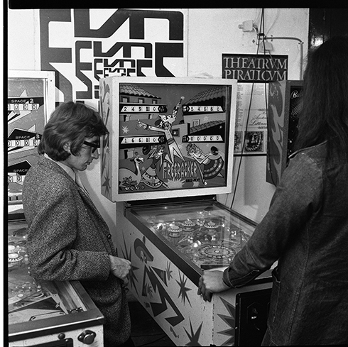 svartvit bild av två människor spelandes vid en pinball maskin