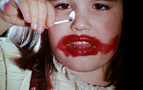Bild av liten flicka med kladdigt rött läppstift som leker med en brinnande tändsticka.