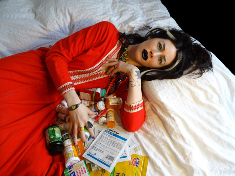 Kvinna i röd dress liggandes på säng med tablettburkar vid handen