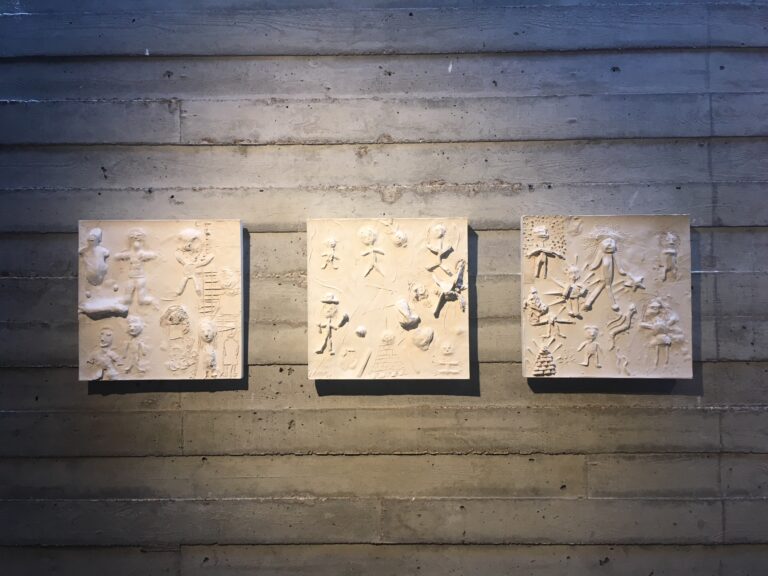 Tre vita reliefplattor mot grå vägg