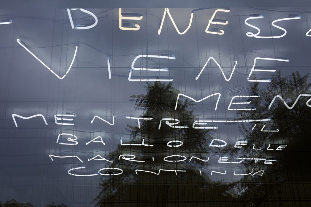 Kvällsbild av ett av Luca Freis verk av lysrör tagen utifrån och in i konsthallen