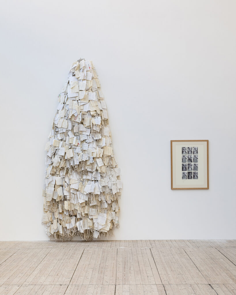 Installation image of a framed picture and a sculpture created from numerous book pages. The sculpture is approximately four meters high