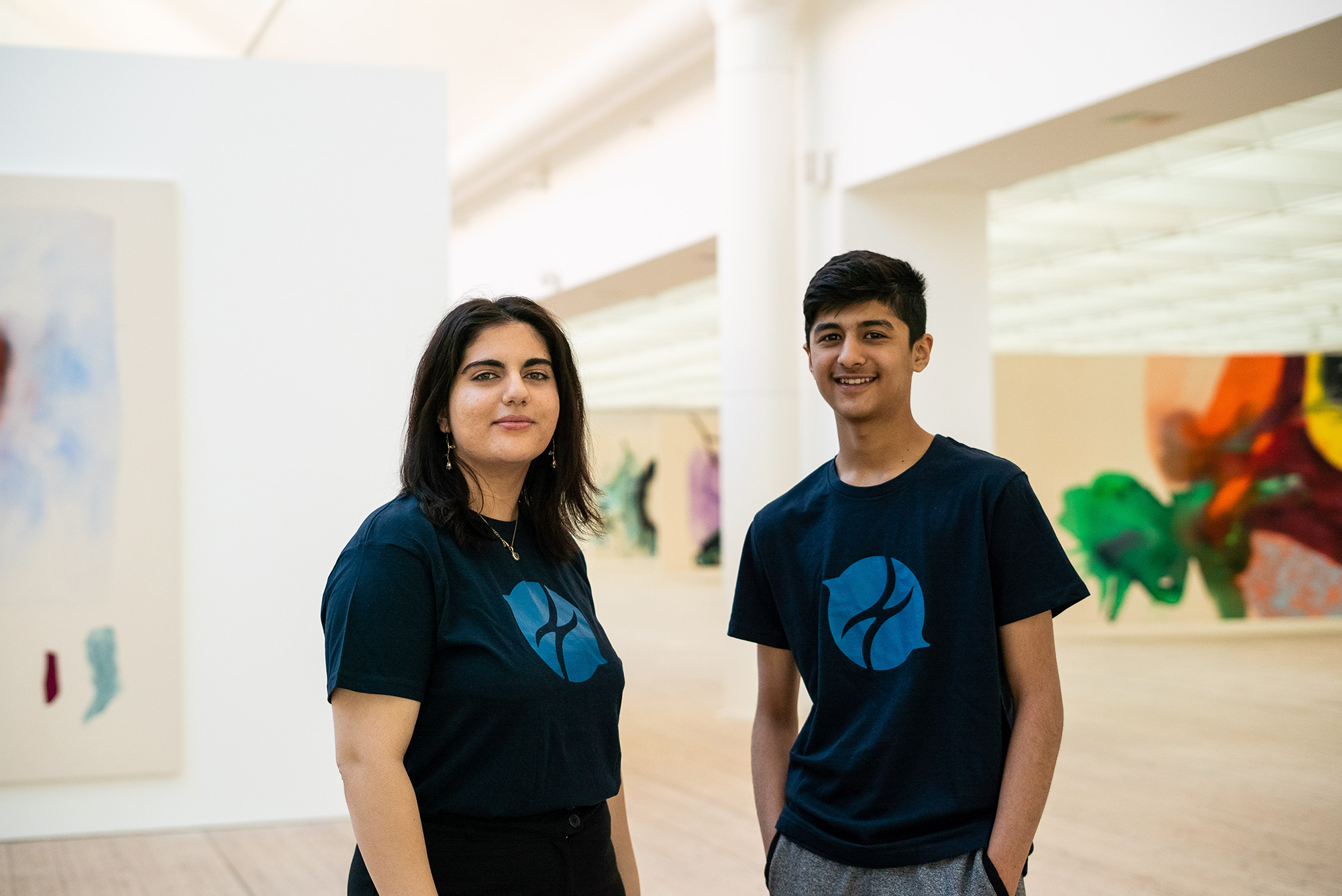 Två personer står i blå tröjor bland konstverk