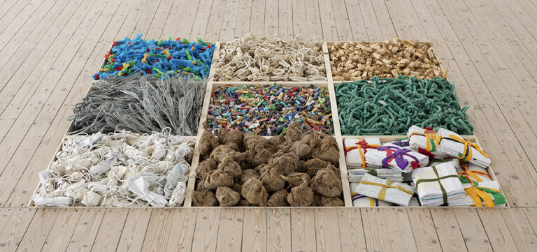 Verk av Hassan Sharif. Lådor med sorterade föremål så som trådstumpar, textilbitar, snören, nedsänkta i konsthallsgolvet.
