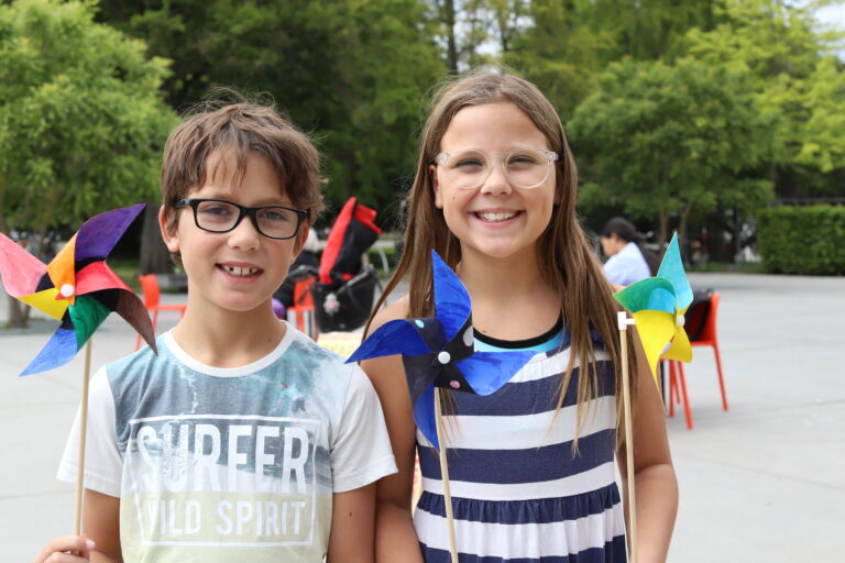 Två barn står med handgjorda vindsnurror utanför konsthallen på sommaren.